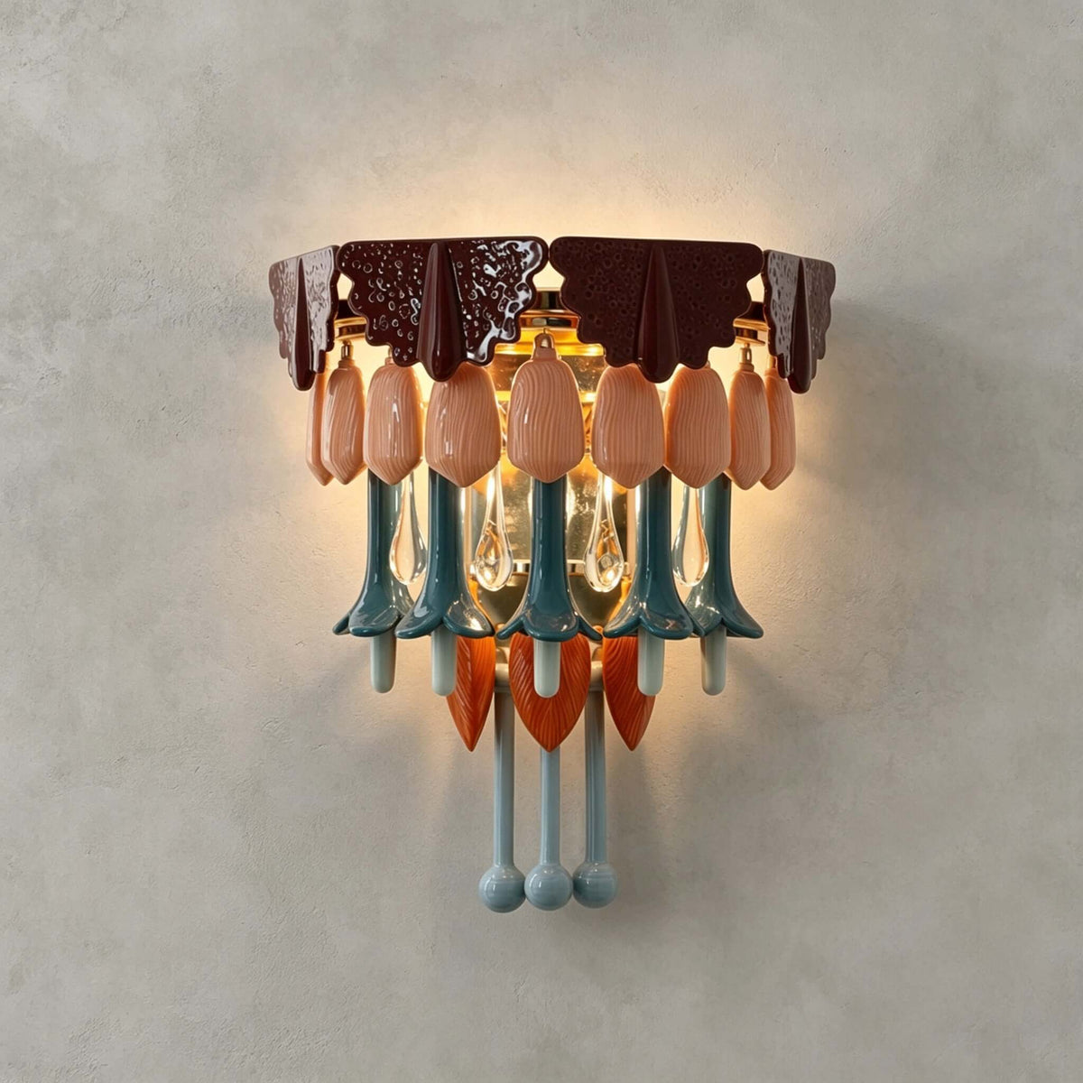 A Clérachic wall sconce lit against a grey plaster wall, showing its burgundy top, pink petals, teal stems and orange accents.