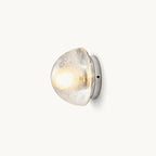 A Clérachic wall light with a clear bubbled-glass dome on a round chrome backplate, lit warm against a plain off-white backdrop.