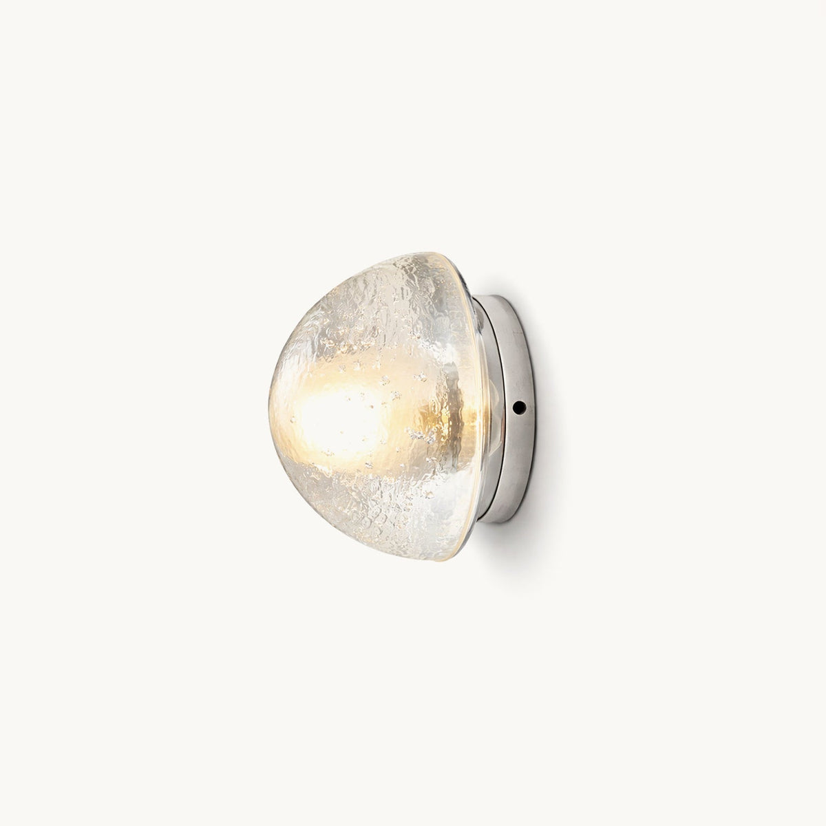 A Clérachic wall light with a clear bubbled-glass dome on a round chrome backplate, lit warm against a plain off-white backdrop.