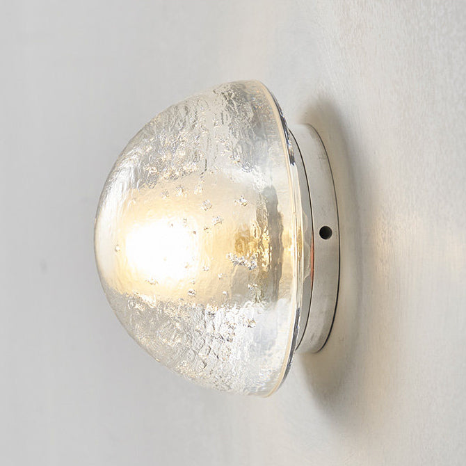 This Clérachic wall lamp seen unlit from the side, the clear dome of rippled, bubble-flecked glass sitting on a slim round plate.