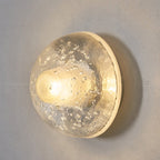 Close view of the lit glass dome on this Clérachic wall lamp, with tiny air bubbles and a warm glow at its centre.