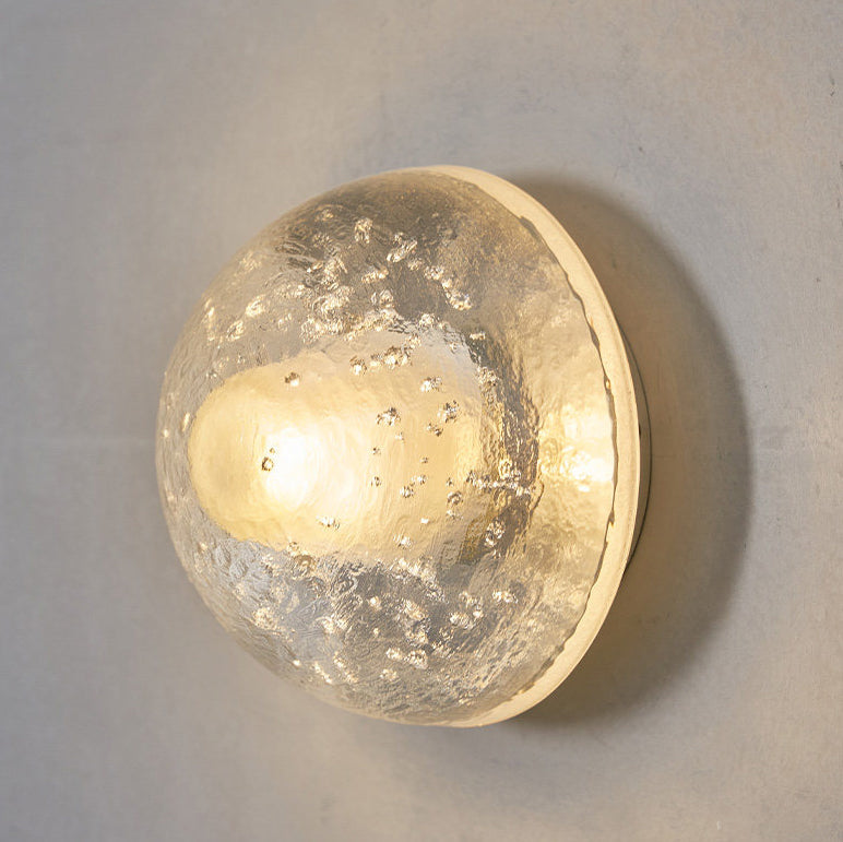 Close view of the lit glass dome on this Clérachic wall lamp, with tiny air bubbles and a warm glow at its centre.