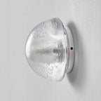 Unlit, the clear glass dome of this Clérachic wall lamp shows its rippled, textured surface and a small screw on the backplate.