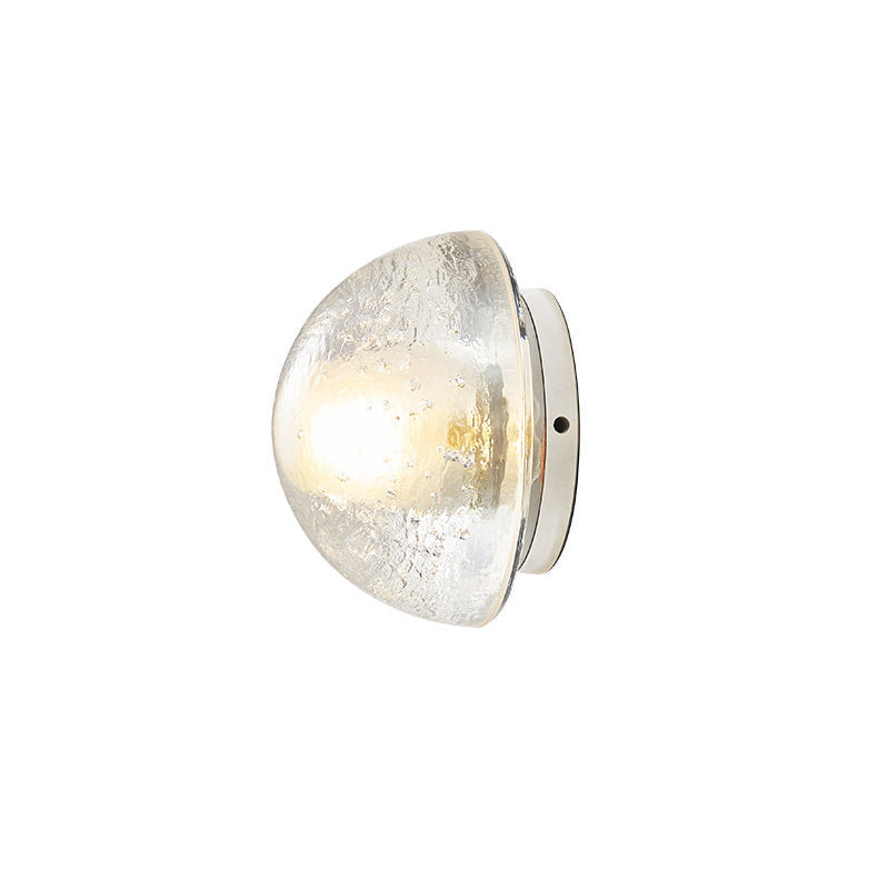 This Clérachic wall lamp on a plain white backdrop, a lit dome of clear bubbled glass on a small round chrome base.