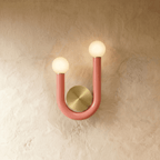 Clérachic U-shaped wall lamp in pink-coral lacquered tube with two frosted globes and a round brushed brass backplate on limewash.