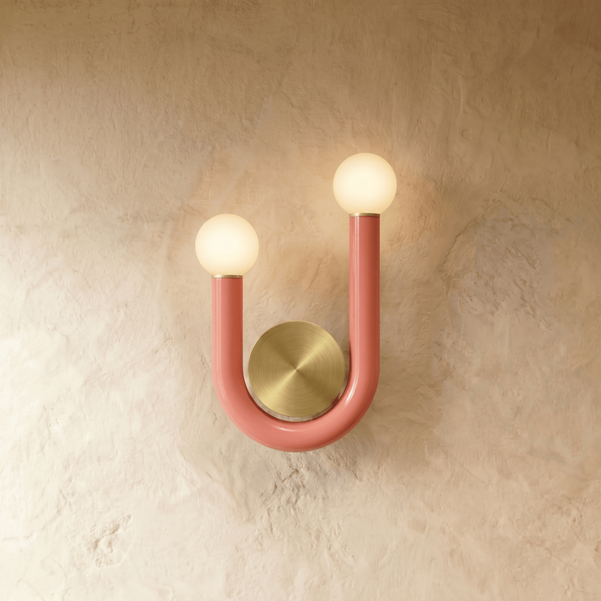 Clérachic U-shaped wall lamp in pink-coral lacquered tube with two frosted globes and a round brushed brass backplate on limewash.