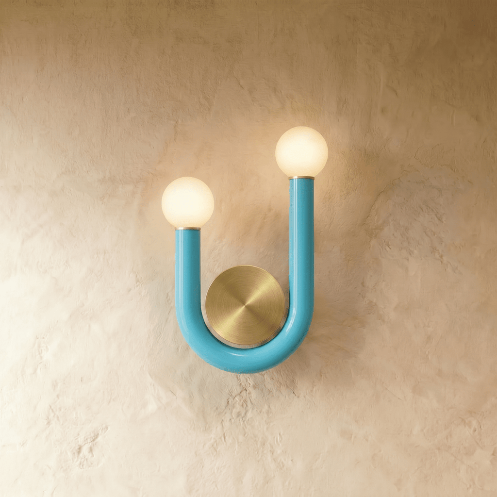 Clérachic U-shaped wall lamp in turquoise blue tube with two glowing opal globes and a brushed brass disc on a plaster wall.