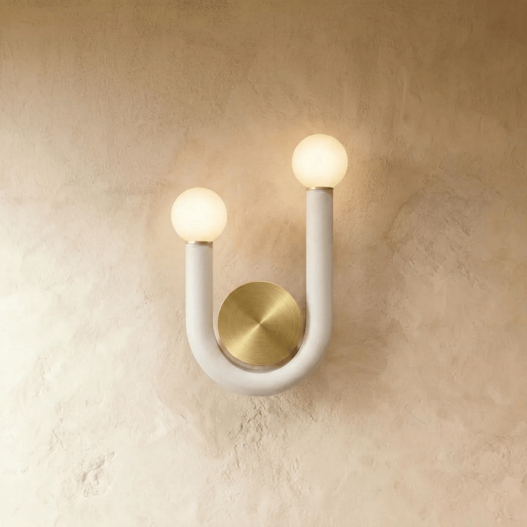 Clérachic U-shaped wall lamp in matte white tube with two frosted globes and a round brushed brass backplate on a limewash wall.