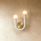 Clérachic U-shaped wall lamp in matte white tube with two frosted globes and a round brushed brass backplate on a limewash wall.