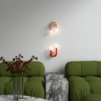 Clérachic pink and red U-shaped wall lamps, one inverted, hung on a pale wall above green boucle sofas and marble side tables.