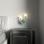 Clérachic turquoise U-shaped wall lamp with two lit globes and a brass disc, fitted on a grey wall beside a bed and steel side table.