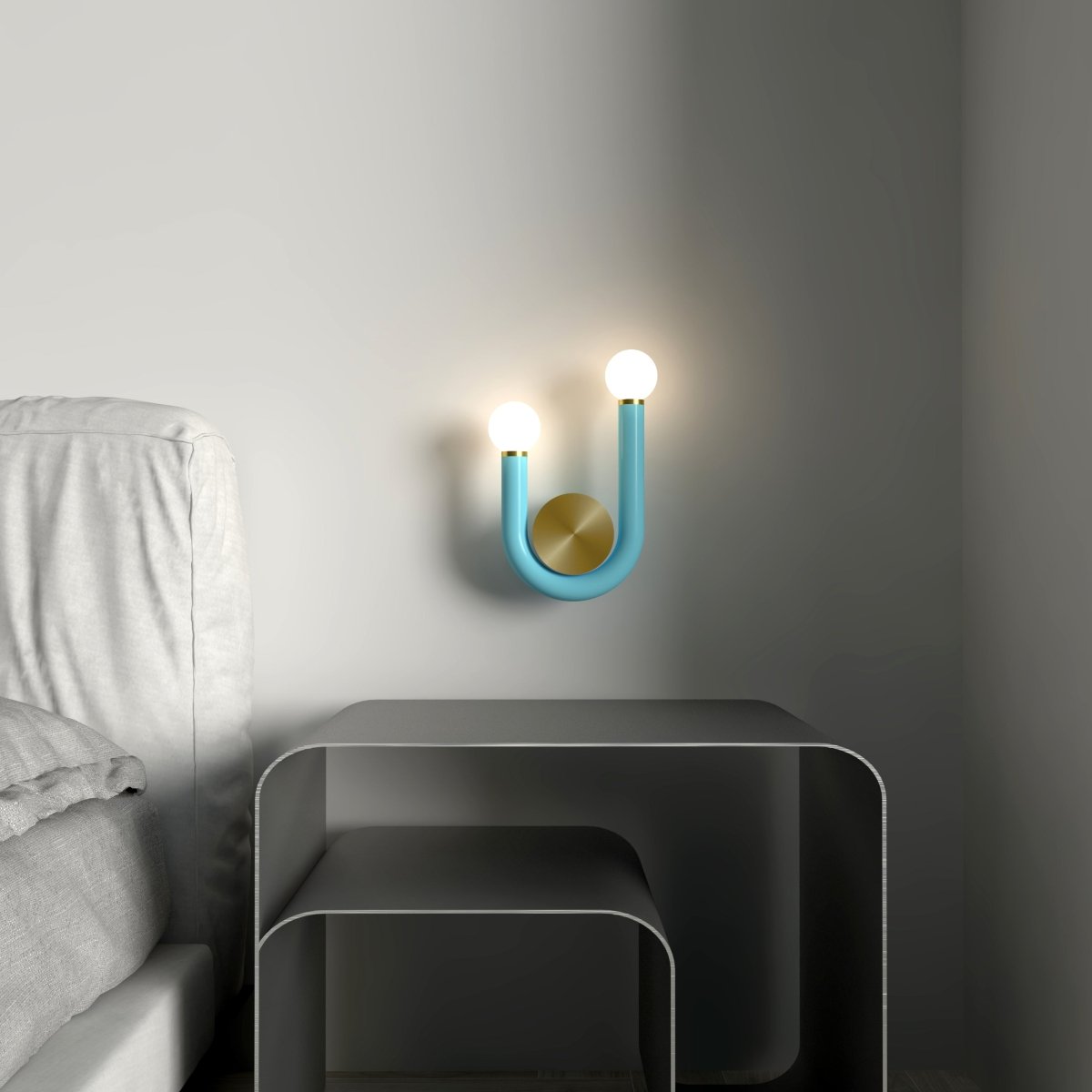 Clérachic turquoise U-shaped wall lamp with two lit globes and a brass disc, fitted on a grey wall beside a bed and steel side table.