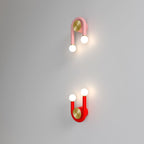 Clérachic pink lamp inverted above a red lamp upright, both U-shaped with lit globes and brass discs on a soft grey wall.