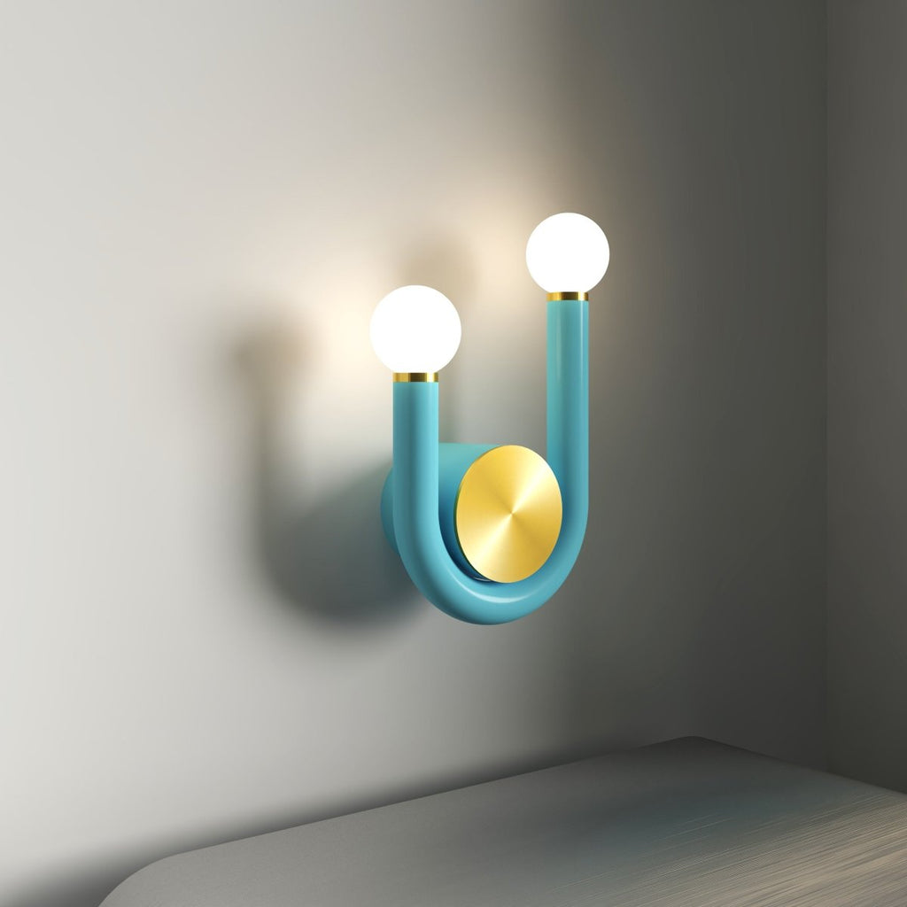 Clérachic turquoise U-shaped wall lamp in close view, two glowing opal globes and a brass disc casting a shadow on a grey wall.