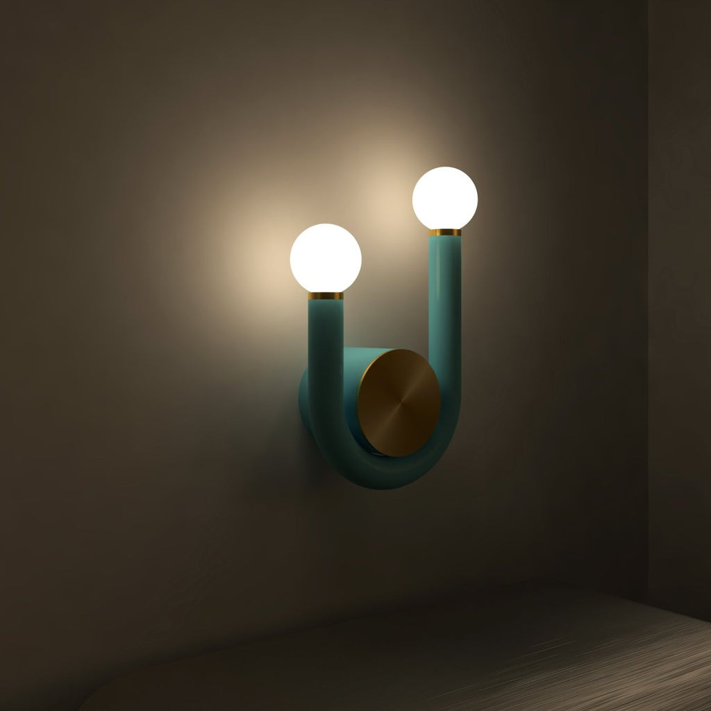 Clérachic U-shaped wall lamp in deep teal tube with two bright opal globes and a brass disc glowing in a dimly lit room.
