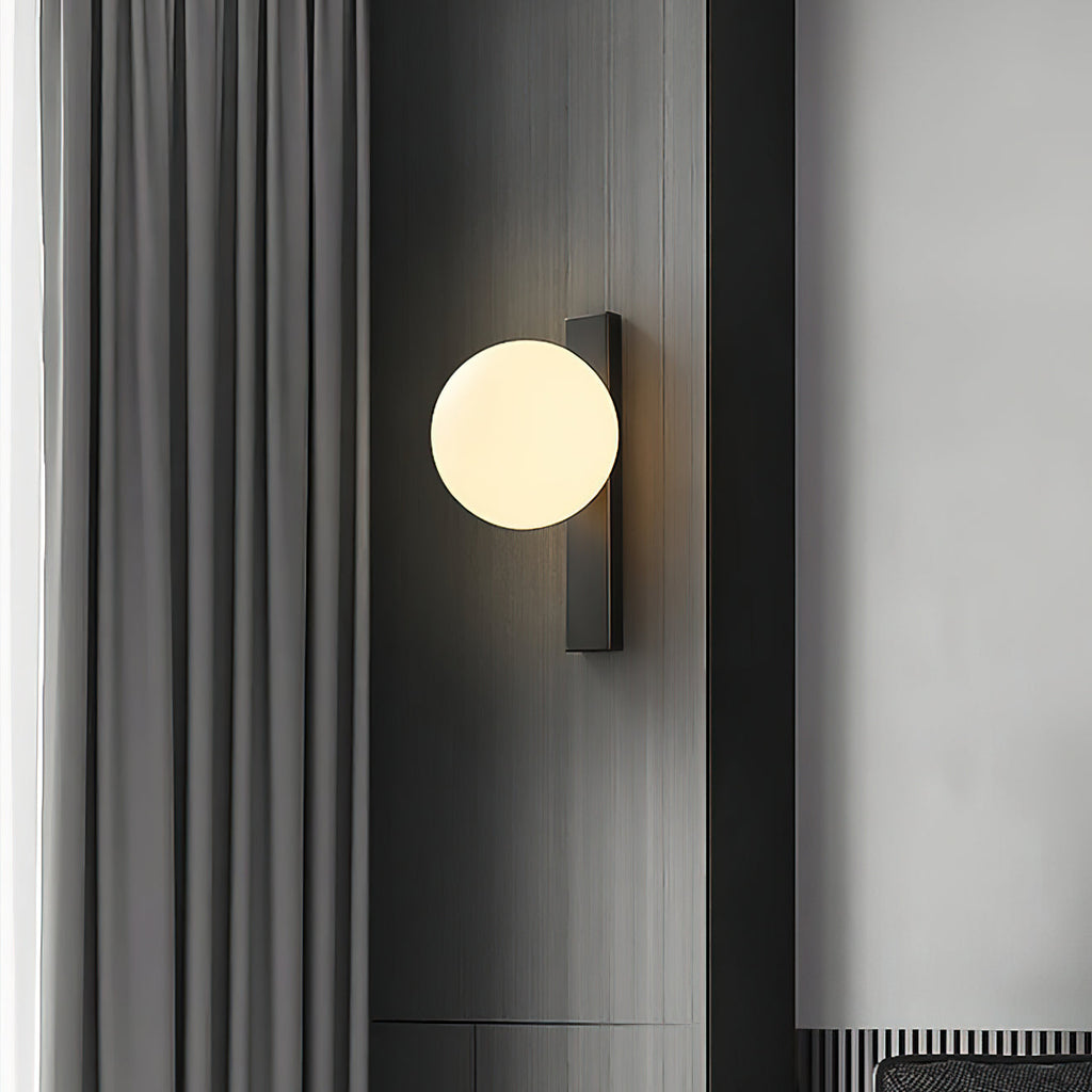 A lit Clérachic wall light with a cream globe on a black bar, mounted on a dark panel beside grey curtains.