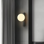 A lit Clérachic wall light with a cream globe on a black bar, mounted on a dark panel beside grey curtains.