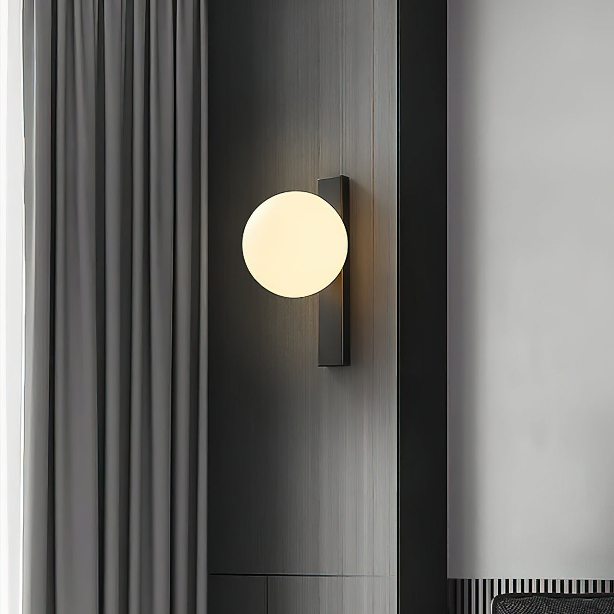 A lit Clérachic wall light with a cream globe on a black bar, mounted on a dark panel beside grey curtains.