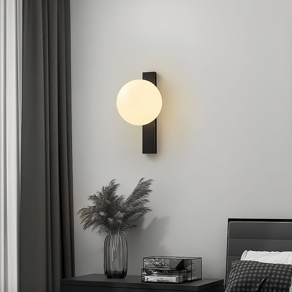 This Clérachic wall light glows above a bedside table with a dried-grass vase, against a pale grey wall and dark curtains.