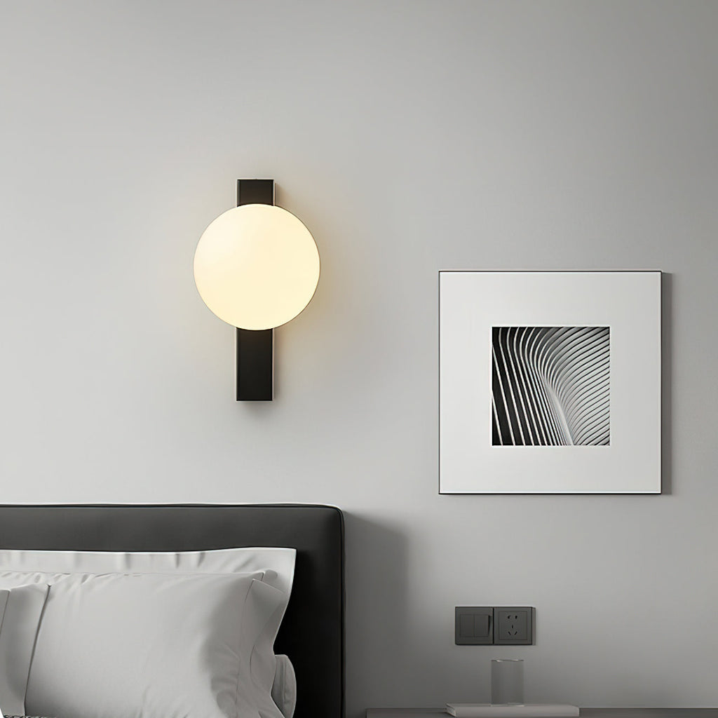 Clérachic wall light with a cream globe on a black bar, lit above a bed, beside a framed black-and-white print.