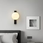 Clérachic wall light with a cream globe on a black bar, lit above a bed, beside a framed black-and-white print.