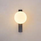Centred on a warm beige wall, the glowing round globe of this Clérachic wall light sits on a slim black bar with a soft halo around it.