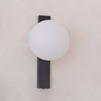 Frosted white globe on a flat black bar, this Clérachic wall light is shown unlit and close to the frame against a pale wall.