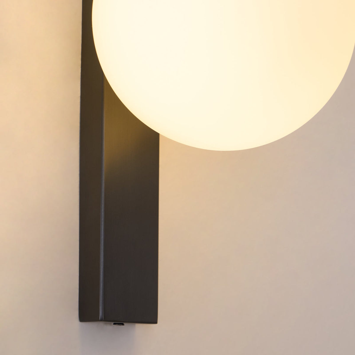 Tight crop of the glowing globe and the square-edged black bar of this Clérachic wall light, with warm light spilling on the wall.