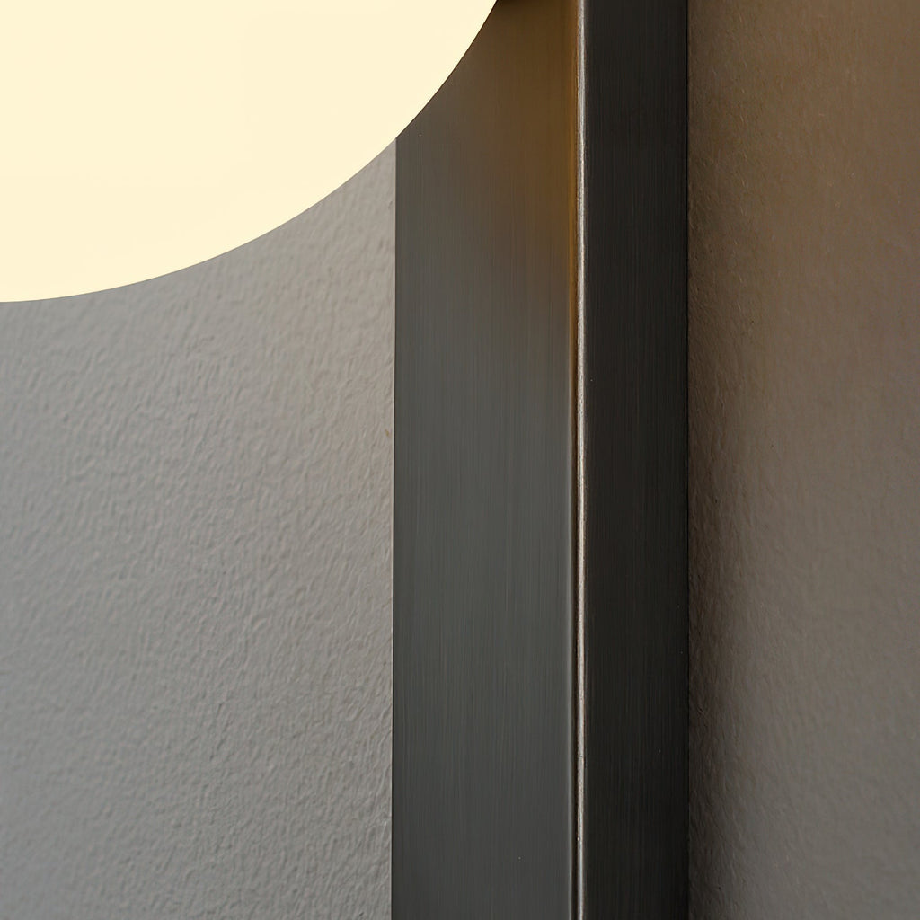 Close view of the brushed dark metal edge of the bar, with the lit globe cut off at the top left of this Clérachic wall light.
