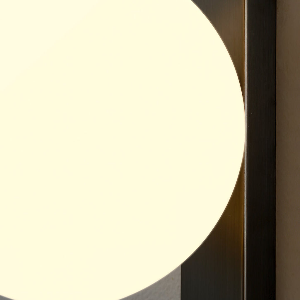 Detail of the lit globe curving past the black metal bar on this Clérachic wall light, filling most of the frame in soft cream light.