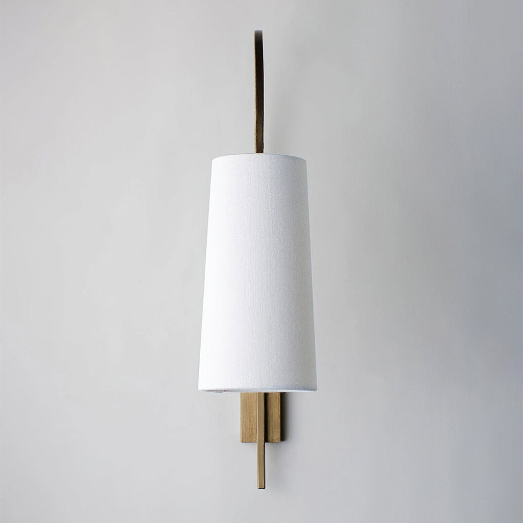 Straight-on view of this Clérachic wall light, with a plain white fabric shade and a slim gold-toned backplate on a pale wall.