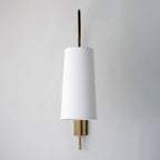 Straight-on view of this Clérachic wall light, with a plain white fabric shade and a slim gold-toned backplate on a pale wall.