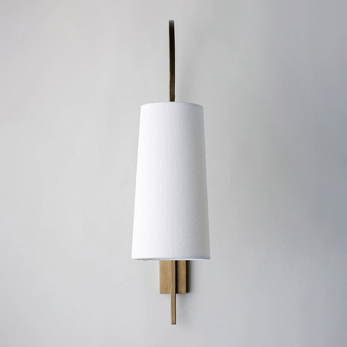 Straight-on view of this Clérachic wall light, with a plain white fabric shade and a slim gold-toned backplate on a pale wall.