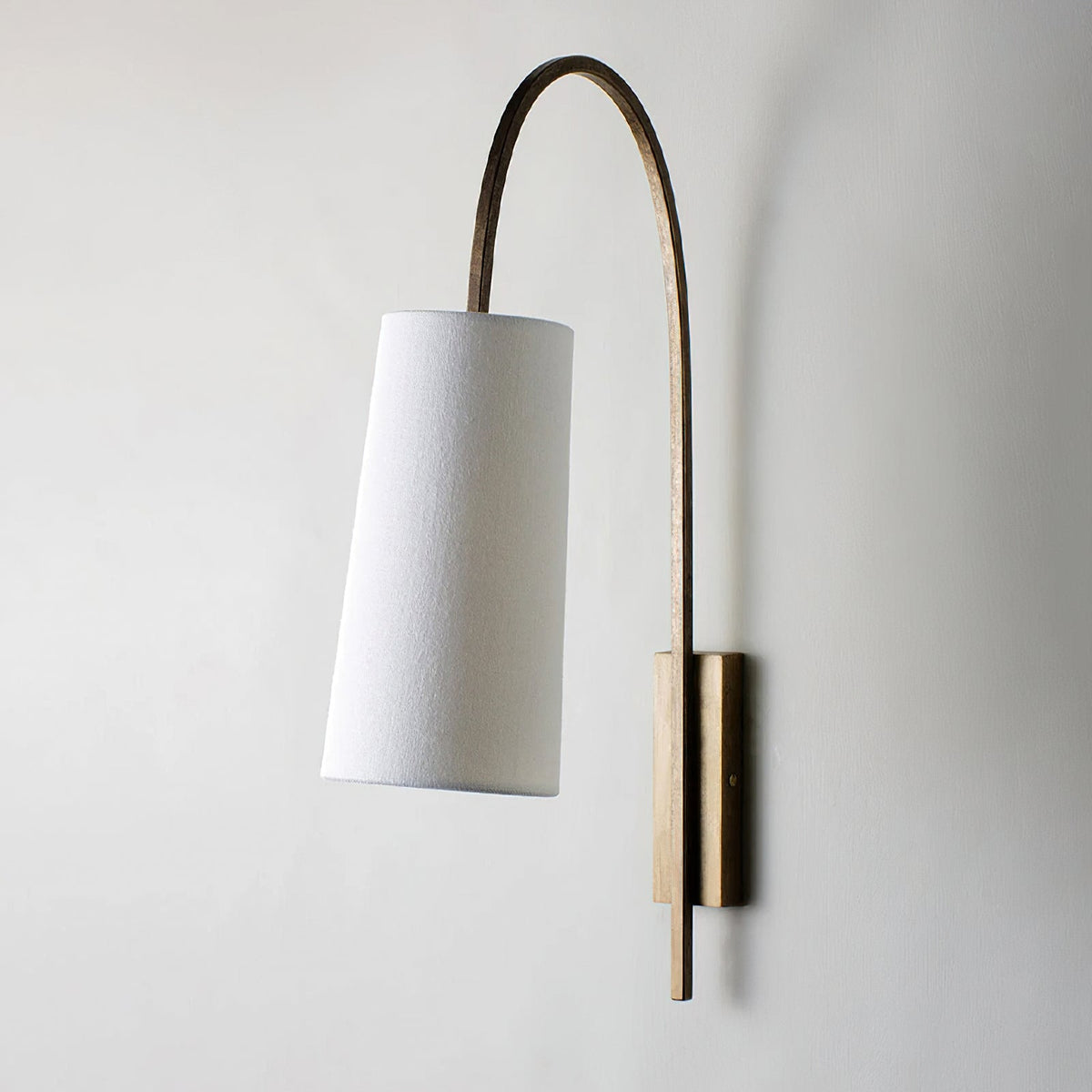 Side view of this Clérachic wall light in gold foil, with a white fabric shade hanging from a long curved arm on a light wall.
