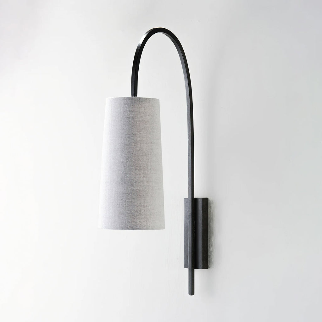 Black iron arm and grey linen-look shade on this Clérachic wall light, unlit, seen side-on against a pale wall.