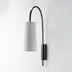 Black iron arm and grey linen-look shade on this Clérachic wall light, unlit, seen side-on against a pale wall.
