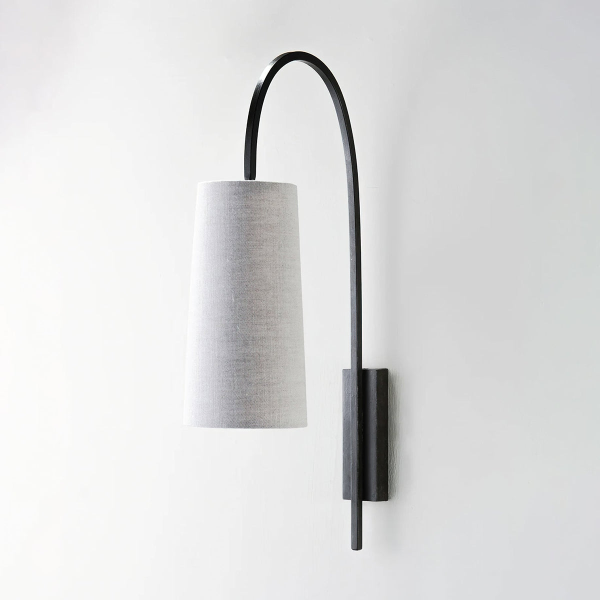 Black iron arm and grey linen-look shade on this Clérachic wall light, unlit, seen side-on against a pale wall.