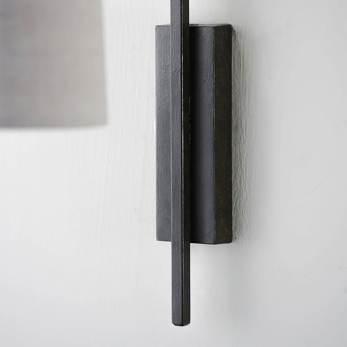Close view of the slim black iron backplate and arm of this Clérachic wall light, with the edge of its shade at the top left.