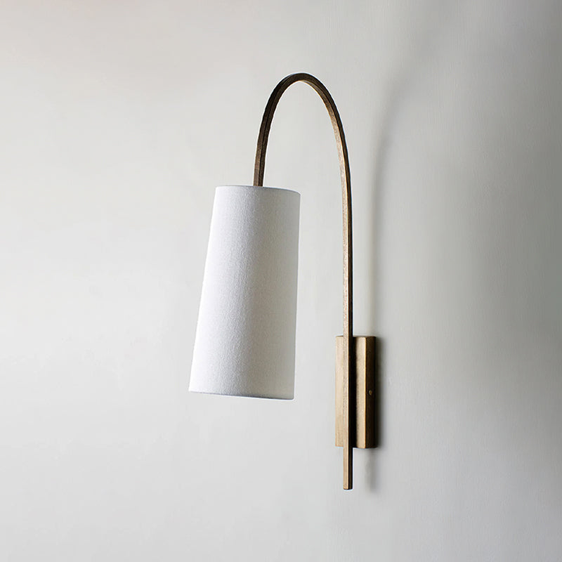This Clérachic wall light with a gold arm and white fabric shade, unlit, hanging on a pale grey wall.