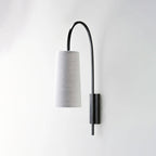 A Clérachic wall light in black iron with a grey fabric shade, its arm arching high over the shade, on a pale wall.