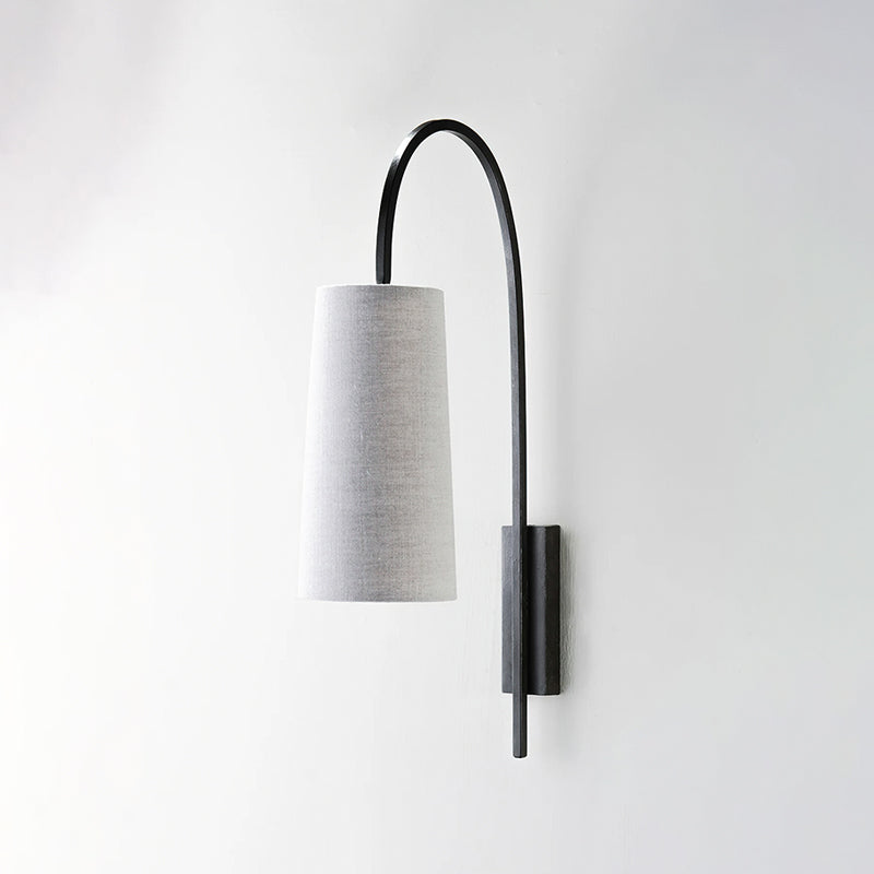 A Clérachic wall light in black iron with a grey fabric shade, its arm arching high over the shade, on a pale wall.
