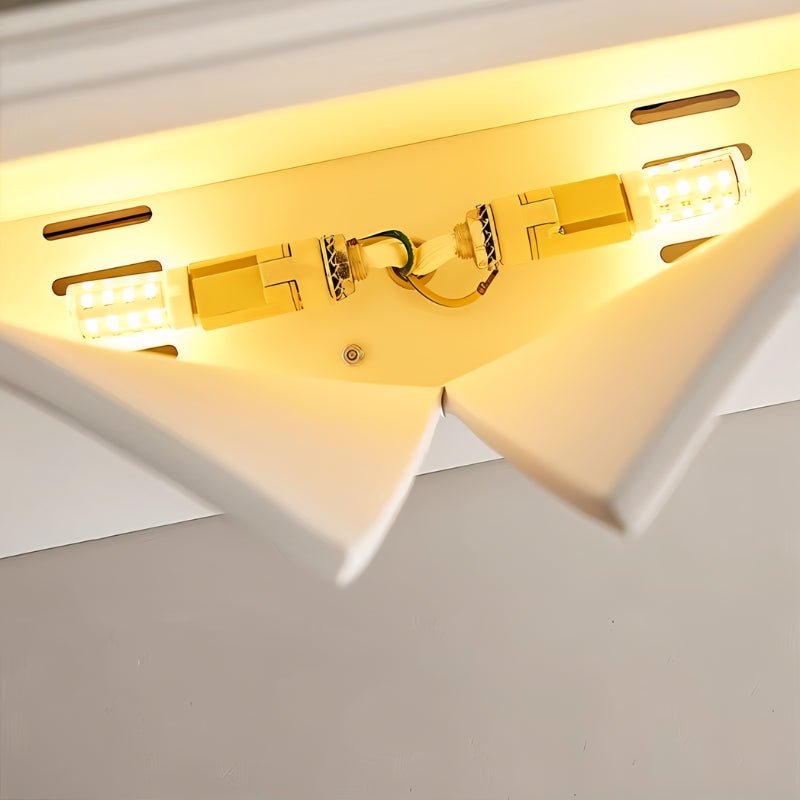 Underside view of a Clérachic white wall light, two bulbs glowing warm inside the curved opening above the central wiring.