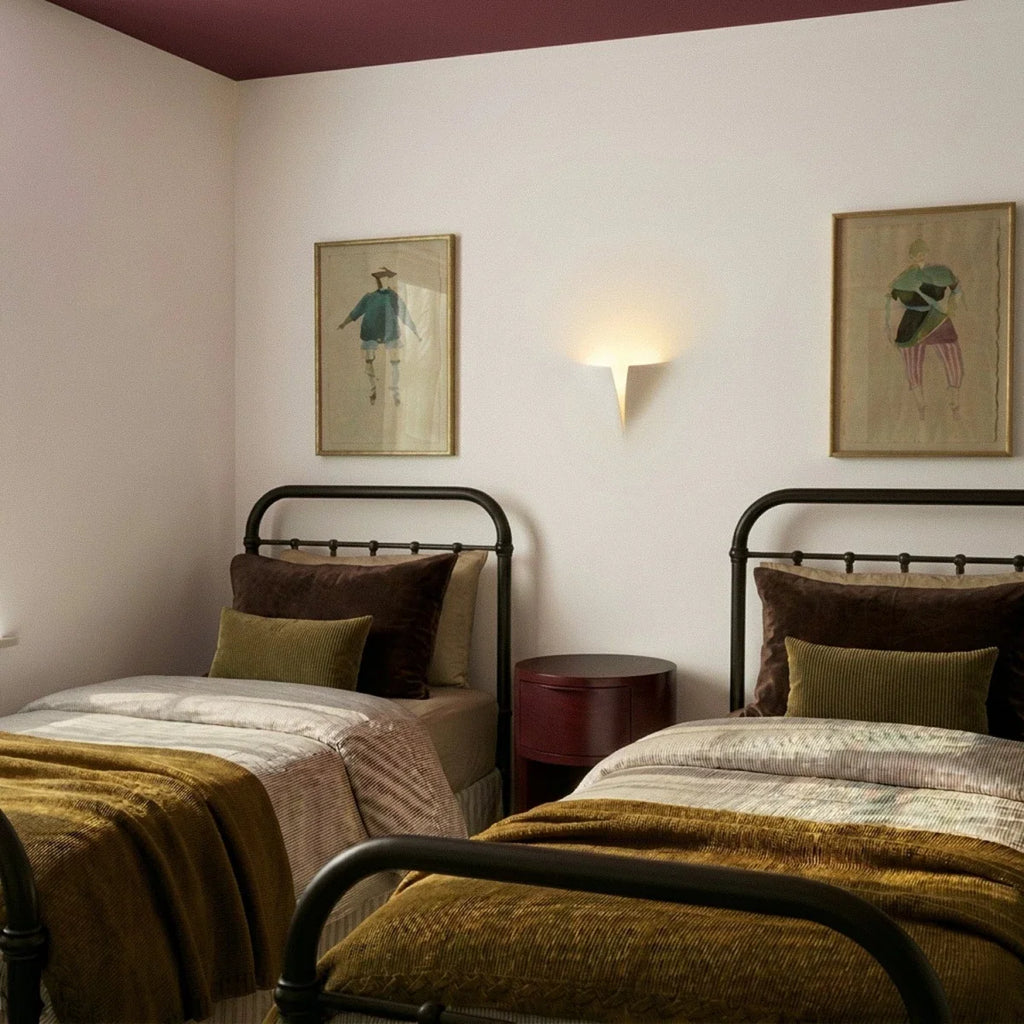 Clérachic white wall light glowing between two framed prints above twin iron-framed beds with olive throws and a burgundy ceiling.
