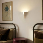 Clérachic white wall light close to a framed print in a bedroom, with iron bed heads and a round burgundy bedside table below.