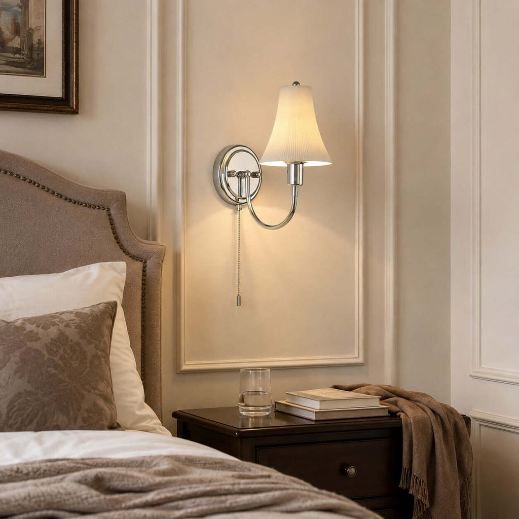 Warm light from the fluted ceramic shade of this Clérachic sconce falls on panelling above a taupe upholstered headboard and a dark nightstand.