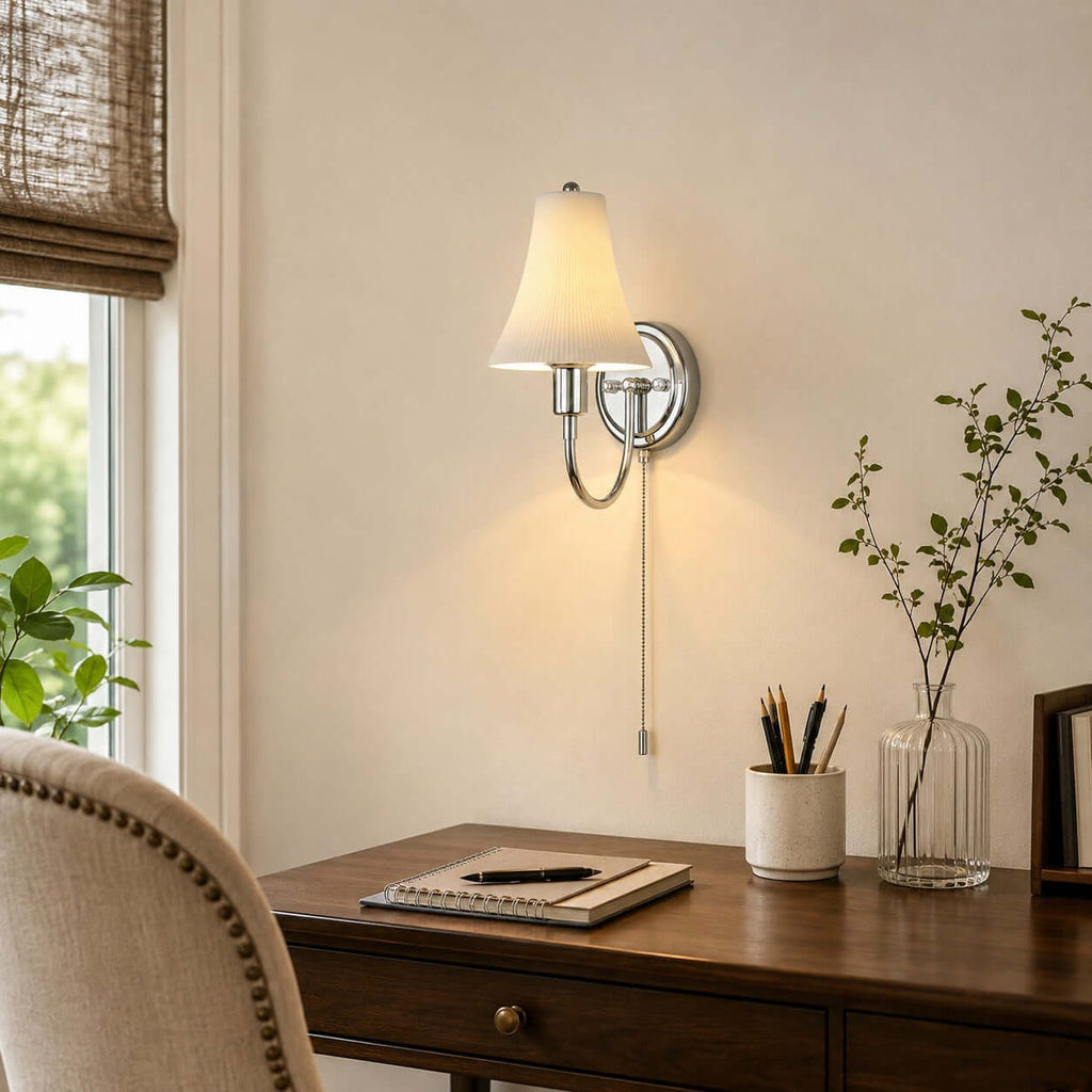 Mounted above a walnut desk with a pencil pot and notebook, this Clérachic sconce lights the wall beside a window and a leafy stem in a glass vase.