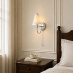 Chrome wall light from Clérachic with a fluted shade over a dark bedside table, where a teacup rests on a book, beside a dark wooden bedpost.