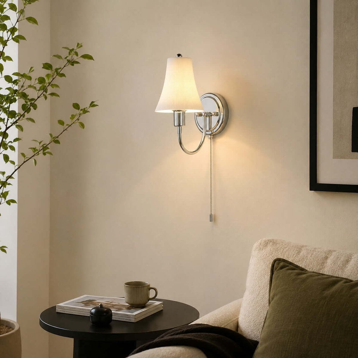 Close to a cream armchair and a round black side table with a cup and magazine, this lit Clérachic wall light glows against a warm beige wall.