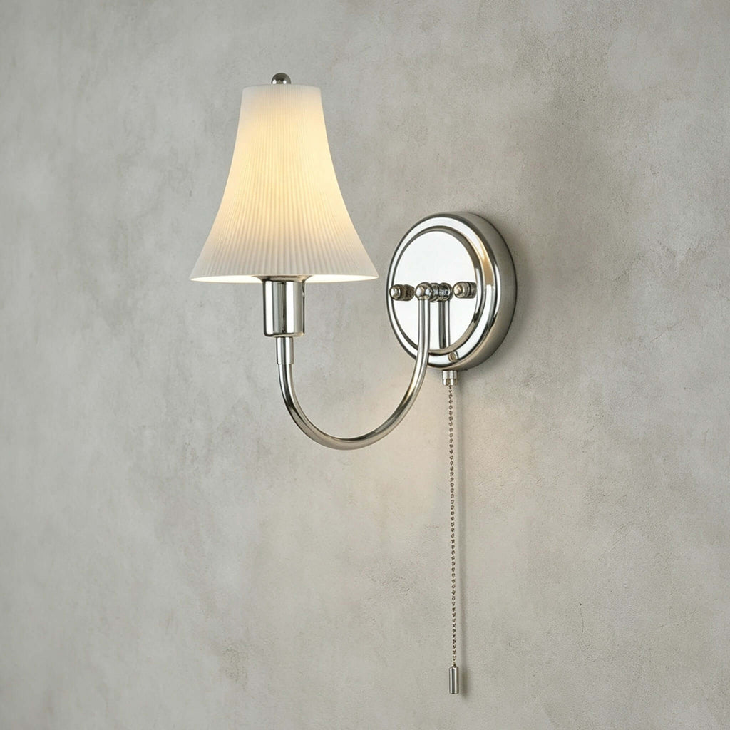 Close view of the fluted ceramic shade, round chrome backplate and beaded pull chain of this Clérachic wall light on textured grey plaster.