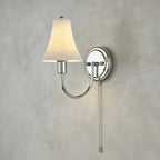 Close view of the fluted ceramic shade, round chrome backplate and beaded pull chain of this Clérachic wall light on textured grey plaster.